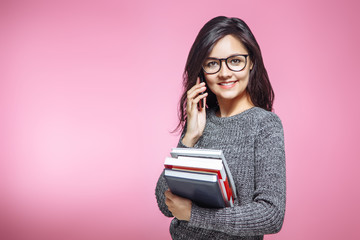 beautiful girl student with books talking on phone on pink background