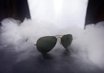 sunglasses on black and light background in smoke, backstage