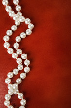 White Pearl Necklace On Red Leather Background.