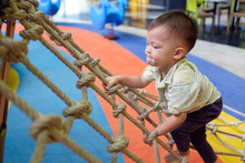 Cute Little Asian 2 Years Old Toddler Baby Boy Child Having Fun Trying To Climb On Jungle Gym At Indoor Playground, Physical, Hand And Eye Coordination, Sensory, Motor Skills Development Concept