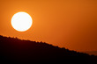 Big sun circle at dusk over mountains with orange sky