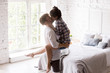 © fizkes - Young happy couple in love spend time together indoors. Husband holding beloved wife on hands kissing in cozy bedroom at home. Just a married, romantic date or celebrate relocate at new house concept