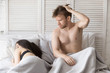 © fizkes - Young millennial married couple lying in bed. Sleeping woman and confused disappointed guy wake up with unknown girl after party hangout have hangover. Problems in sexual life or impotence concept