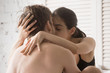 © fizkes - Young millennial attractive couple in love on bed in bedroom foreplay at home. Shirtless man kissing an excited seductive girl. Romantic relationships tenderness and feelings. Passion and sex concept