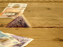 British Bank Notes Between Wooden Pine Floor Boards, Showing A Corner Peep Of The Currency In The Gap.