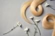 Composition with locks of blond hair and flowers on color background, flat lay