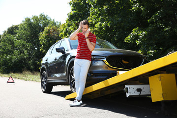 Man talking on phone near broken car and tow truck outdoors