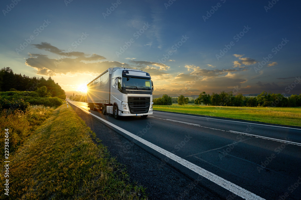 White truck driving on the asphalt road in rural landscape in the rays of the sunset - obrazy, fototapety, plakaty 