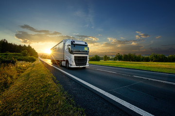 Wall Mural - white truck driving on the asphalt road in rural landscape in the rays of the sunset