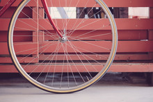 Front Wheel Of A Red Bicycle Against A Fence Wall.