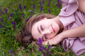 a portrait of a young teenager girl with long curled hair dressed in pink lying in the grass with flowers