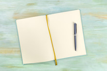 A top shot of an open journal with a pen on a teal blue background with a place for text