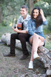 © soleg - young couple sitting on a log in the forest and playing guitar, summer nature, romantic feelings