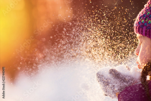 Obraz Dibond Baby girl blowing snow in frosty winter park. Flying Snowflakes. Sunny day. Backlit. Child to have fun outdoors