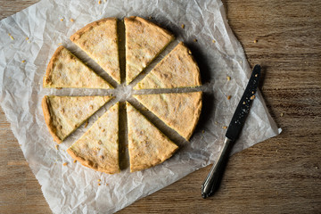 Zitronenkuchen in gleich große Stücke geschnitten symmetrisch platziert auf weißem Backpapier und braunem Untergrund von oben bei Tageslicht fotografiert