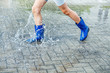 girl in blue rubber boots jumping in a puddle after a rain