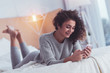 Relaxed woman. Relaxed young woman feeling relieved while lying in bed holding her phone in her hands