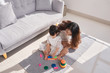 © makistock - Happy loving family. Mother and daughter are doing play a toy and having fun. Mother and daughter doing your education sitting on the floor in the living room.