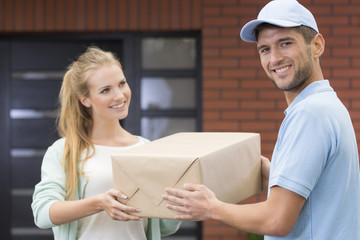 Wall Mural - Young girl taking a delivery form handsome courier in blue uniform