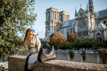 Wall Mural - Young woman tourist sitting near the famous Notre Dame cathedral during the morning light traveling in Paris, France