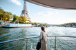 Young woman enjoying beautiful landscape view on the riverside with Eiffel tower from the boat during the sunset in Paris