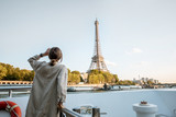 Fototapeta Paryż - Young woman enjoying beautiful landscape view on the riverside with Eiffel tower from the boat during the sunset in Paris