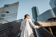 © rh2010 - Stylish businesswoman in white suit going up on the escalator at the business centre outdoors with skyscrapers on the background in Paris