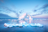 Photogenic and intricate iceberg with a hole under an interesting and colorful sky during sunrise with full moon. Disko bay, Greenland.