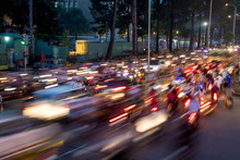 Dense traffic at night intersection with blurred lights passing through motorbikes and vehicles.