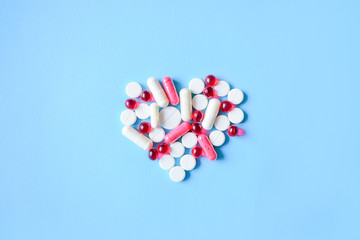 White and red various pills and capsules in heart  shape on blue background. Concept medical treatment, Medicine for diabetes, heart diseases and High blood pressure.