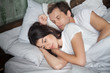 © fizkes - Young attractive couple lying in bed under blanket at home. Male sleeping, pensive sad and frustrated female thinking about relationships or treason. Problems in sexual life or childlessness concept
