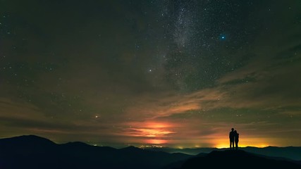 Wall Mural - The man and a woman standing on a mountain with stars background. time lapse