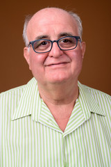 Overweight senior man wearing eyeglasses against brown backgroun