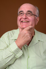 Overweight senior man wearing eyeglasses against brown backgroun