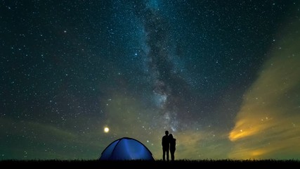 Wall Mural - The man and a woman near a camping tent standing on a meteor shower background