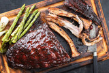 Barbecue spare ribs St Louis cut with hot honey chili marinade and green asparagus as top view on an old rustic board