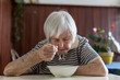 Solitary senior woman eating her lunch at retirement home. Social aid for retirement citizens concept.