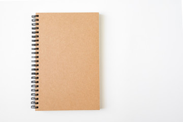 top view of closed spiral blank craft paper cover notebook with pencil on white desk background