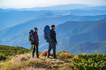 the man and a woman with backpacks standing on the mountain