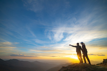 Wall Mural - the couple gesturing on the mountain with a picturesque sunset background