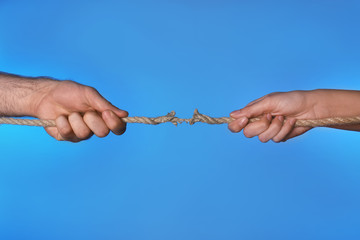 Wall Mural - Woman and man pulling damaged rope on color background