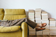 © JacquiMiller/Stocksy - Female resting on retro yellow sofa with stacks of books in background