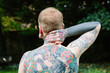 © kkgas/Stocksy - Outdoor portrait of a heavily tattooed man with distinctive ear stretch and tattoo design photographed from behind to show the back tattoo and arms