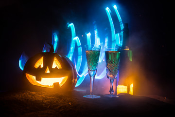 Two glasses of wine and bottle with Halloween - old jack-o-lantern on dark toned foggy background. Scary Halloween pumpkin