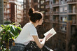© Bonninstudio/Stocksy - Side view of a young woman reading a book in a balcony.