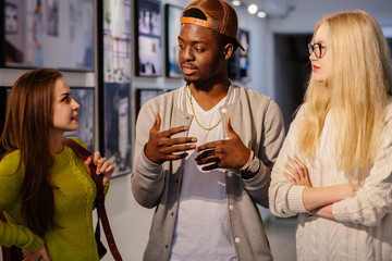 young black hipster man talking and gesticulating with two girl friends in art photo gallery. multi 