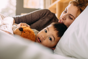 Little boy in bed with his teddy and mother