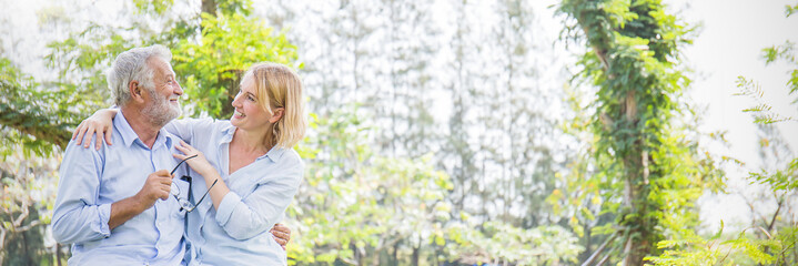 Happy old couple smiling in a park on a sunny day, hoot senior couple relax in the forest spring summer time. Healthcare lifestyle retirement concept banner