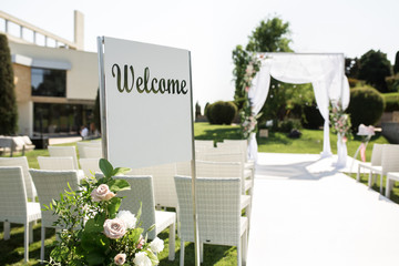 Wall Mural - Outdoor wedding ceremony. Welcome plate decorated with fresh flowers on wedding chuppa background