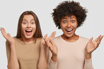 Photo of emotive females gesture with palms, react to awesome news, meet foreign friend, isolated over white background. Amazed dark skinned young woman has Afro haircut spends free time with fellow